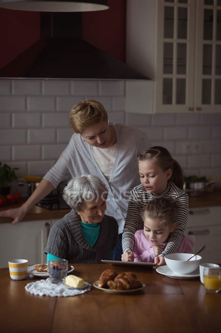 Семья из нескольких поколений, использующая цифровую тарелку на кухне дома — стоковое фото