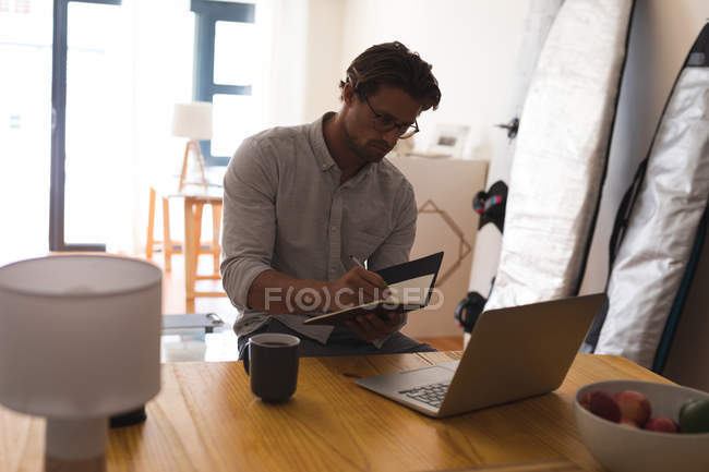 Man writing on a diary while using laptop at home — Stock Photo
