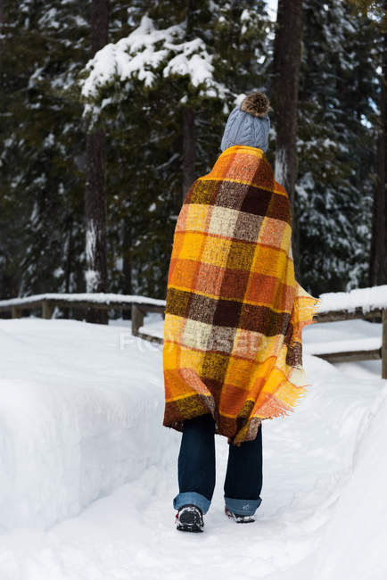 Человек, завернутый в одеяло, ходит зимой по снежному лесу — стоковое фото