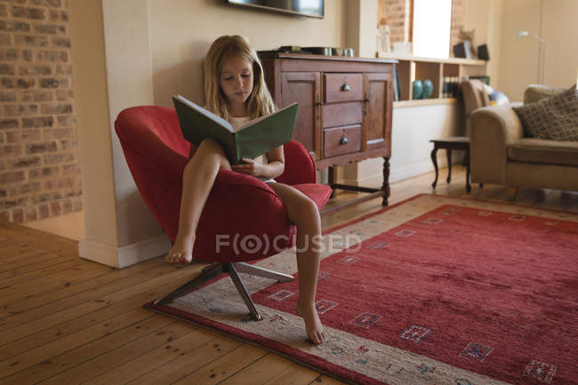 Chica estudiando en casa y sentada en sillón con libro - foto de stock