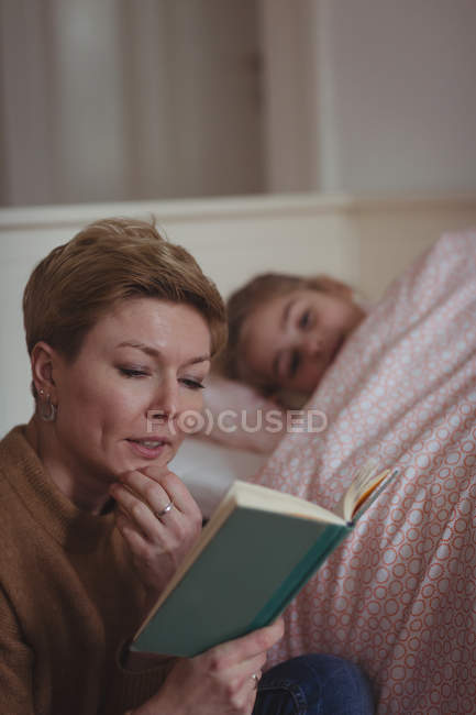 Mother reading a book while girl sleeping in bedroom at home — Stock Photo