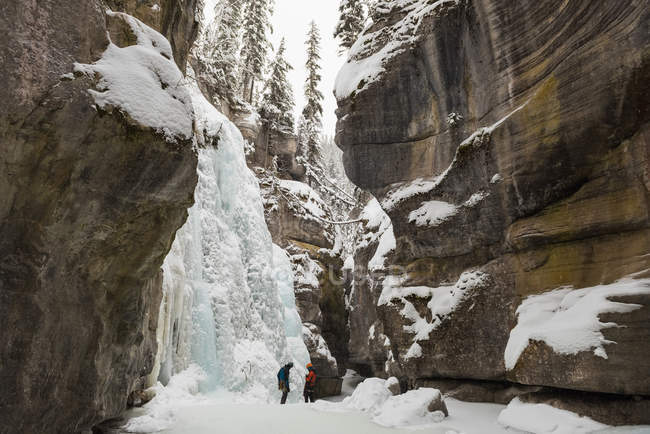 Casal de pé juntos perto da montanha rochosa durante o inverno — Fotografia de Stock