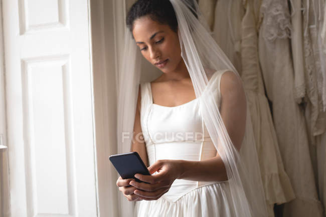 Jovem noiva em vestido de noiva usando telefone celular na boutique — Fotografia de Stock