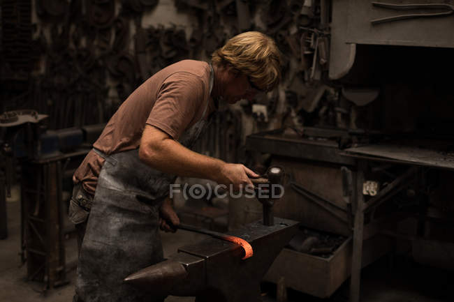 Blacksmith hammering a hot metal rod in workshop — Stock Photo