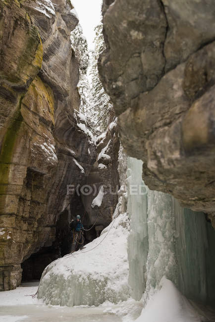 Male climber standing near rocky ice mountain during winter — Stock Photo
