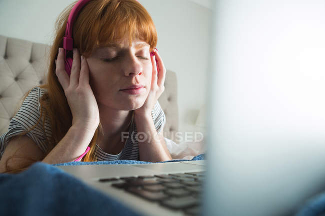 Женщина с наушниками слушает музыку в спальне дома — стоковое фото