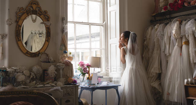 Жінка змішаної раси, наречена в білій сукні дивиться через вікно на старовинному бутіку — стокове фото