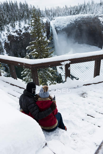 Paar in warmer Kleidung schaut sich im Winter Wasserfall an — Stockfoto