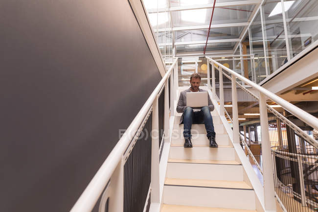 Businessman using laptop on staircase at office — Stock Photo