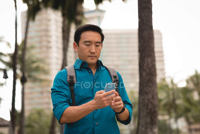 Lässiger erwachsener Mann mit Rucksack kontrolliert Handy auf der Stadtstraße — Stockfoto