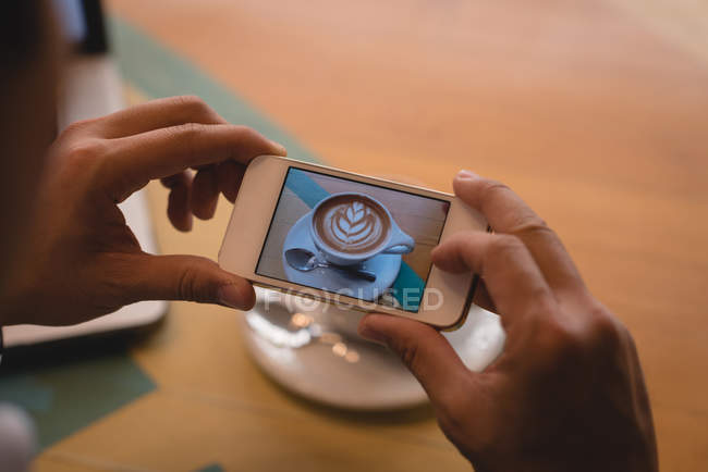 Close-up of businessman clicking photo of coffee in coffee shop — Stock Photo