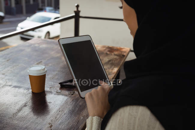 Primer plano de la mujer hijab usando tableta digital en la cafetería - foto de stock