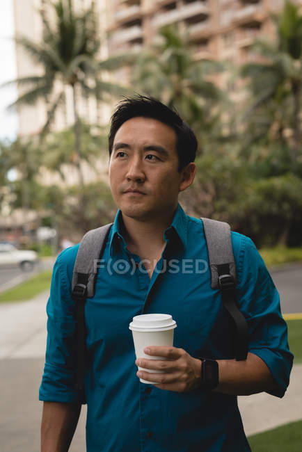 Homme intelligent marchant avec tasse jetable dans la rue de la ville — Photo de stock