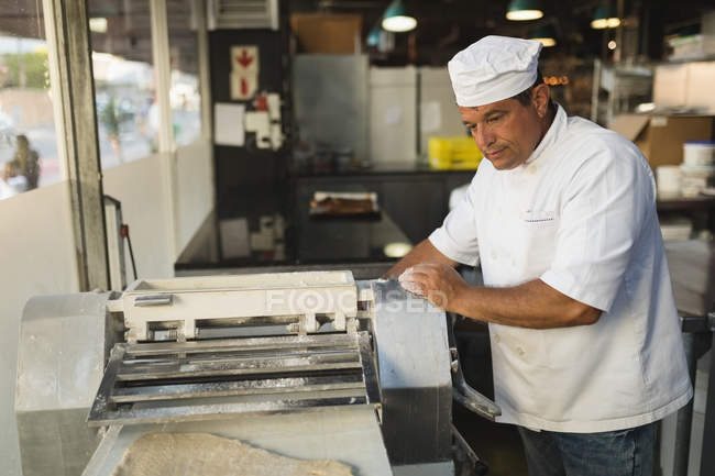 Mature male baker using machine in bakery shop — Stock Photo