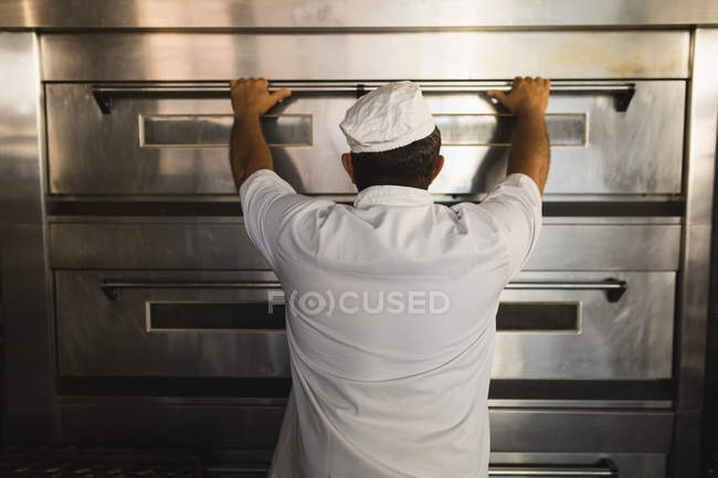 Rear view of male baker using baking owen in bakery shop — Stock Photo