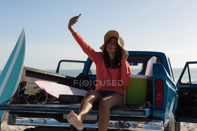 Woman taking selfie with mobile phone in a pickup truck at beach — Stock Photo