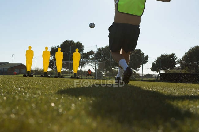 Jogador chutando futebol no campo de esportes em um dia ensolarado — Fotografia de Stock