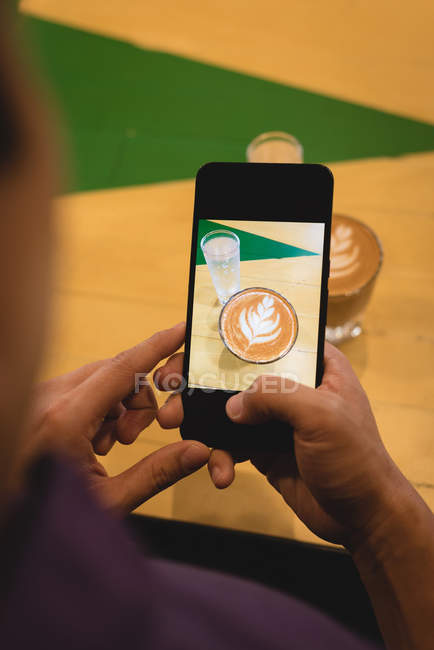 Mann klickt auf Foto von Kaffee mit Handy im Café — Stockfoto
