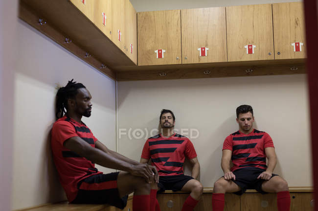 Jugadores de fútbol relajándose en el banco en el vestidor - foto de stock