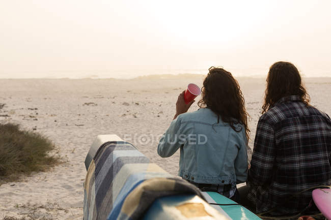 Vista trasera de la pareja tomando algo en una camioneta en la playa - foto de stock