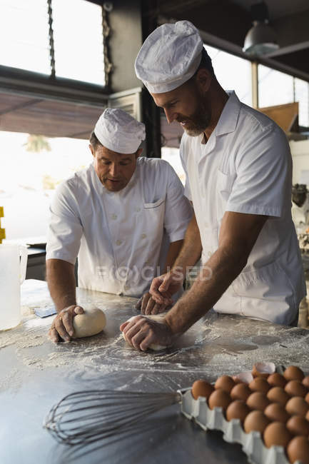 Hombre panadero preparando la masa con su compañero de trabajo - foto de stock