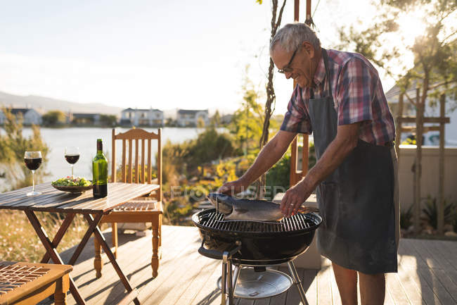 Старший мужчина готовит рыбу на барбекю на заднем дворе — стоковое фото
