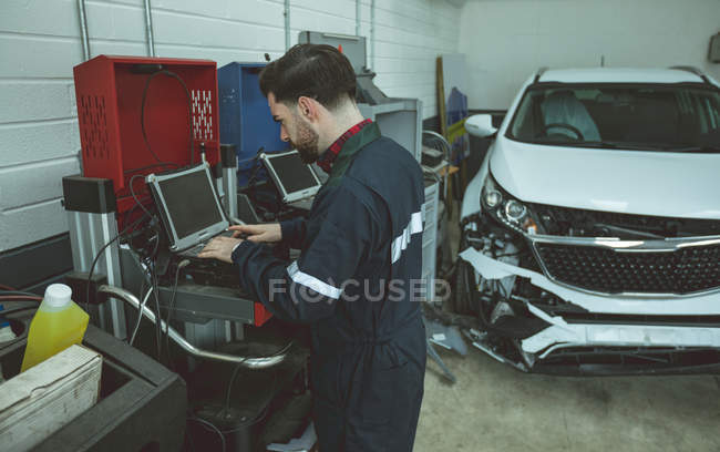Mécanicien utilisant un ordinateur portable tout en réparant la voiture dans le garage — Photo de stock