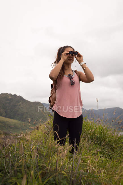 Mulher bonita olhando através de binóculos no campo — Fotografia de Stock