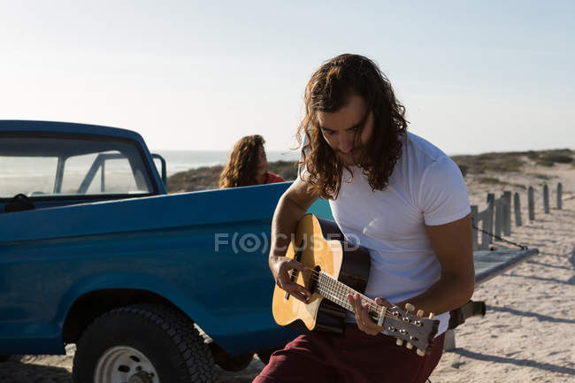 Homme jouant de la guitare à la plage par une journée ensoleillée — Photo de stock
