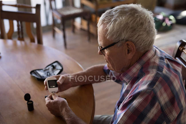 Hombre mayor revisando su azúcar en sangre con glucosímetro en casa - foto de stock