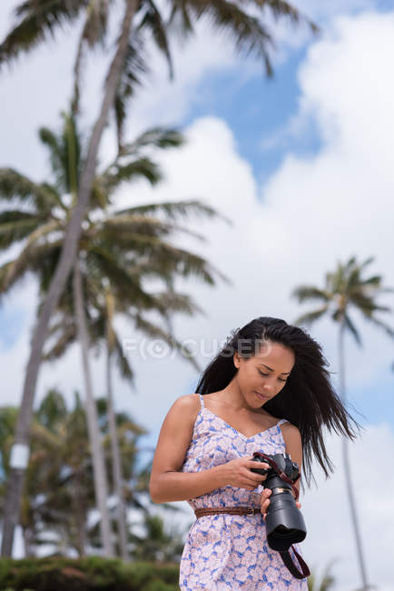 Молодая женщина рассматривает фотографии на цифровой камере на пляже — стоковое фото