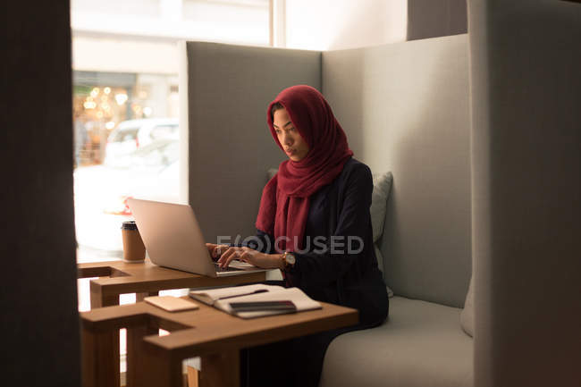 Businesswoman in hijab using laptop at office cafeteria — Stock Photo