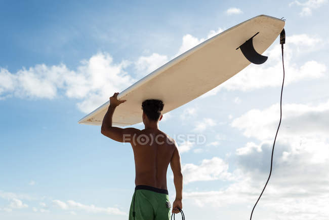 Vista trasera del surfista masculino caminando con tabla de surf en la playa - foto de stock