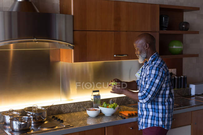 Uomo anziano preparare insalata in cucina a casa — Foto stock