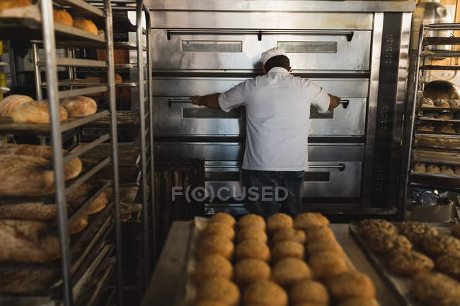 Rear view of male baker using baking owen in bakery shop — Stock Photo