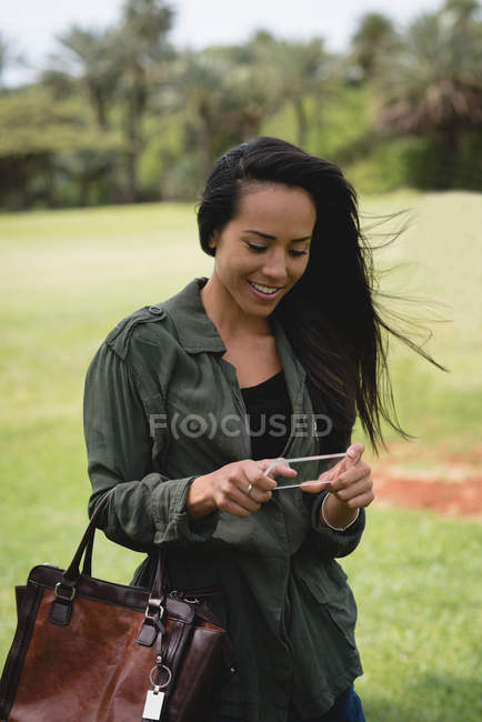 Mulher sorridente usando telefone celular de vidro no parque — Fotografia de Stock
