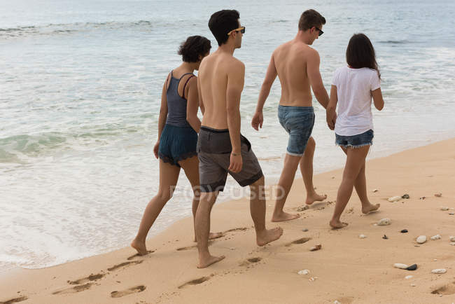 Due coppie che camminano mano nella mano sulla spiaggia — Foto stock