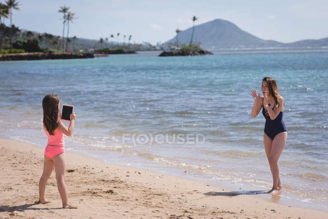 Дочь нажав фото матери с цифровым планшетом на пляже — стоковое фото