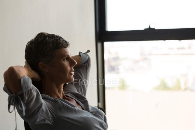 Reife Geschäftsfrau entspannt sich mit den Händen hinter dem Kopf und sitzt im Büro auf einem Stuhl — Stockfoto