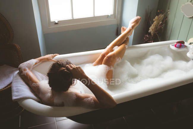 Женщина принимает ванну с пеной в ванной комнате дома — стоковое фото