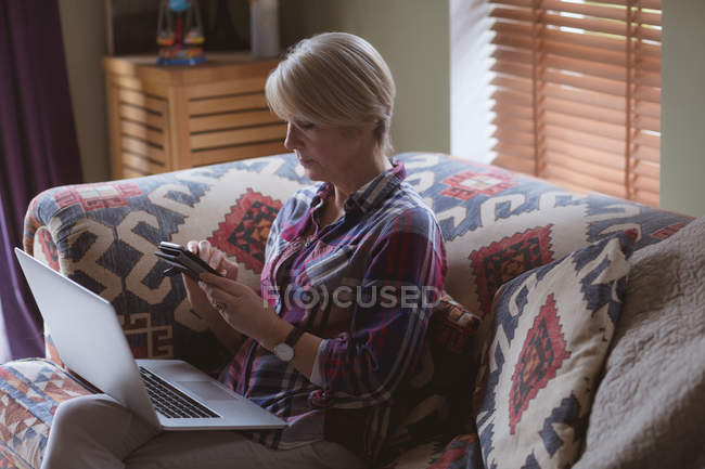 Mulher madura usando telefone celular no sofá na sala de estar em casa — Fotografia de Stock