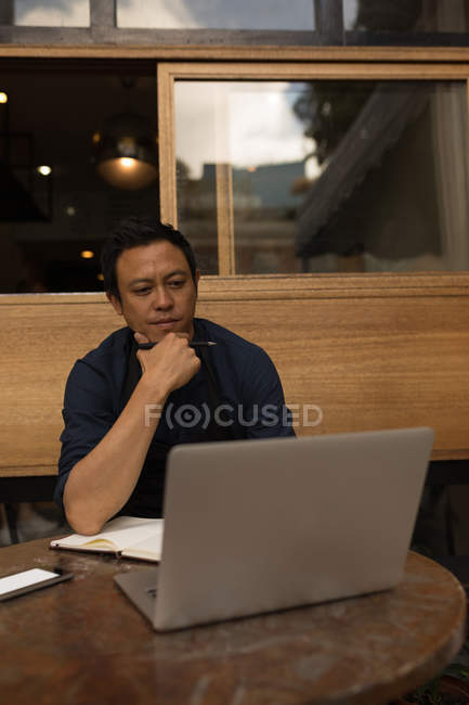 Продуманий бізнесмен дивиться на ноутбук у тротуарному кафе — стокове фото
