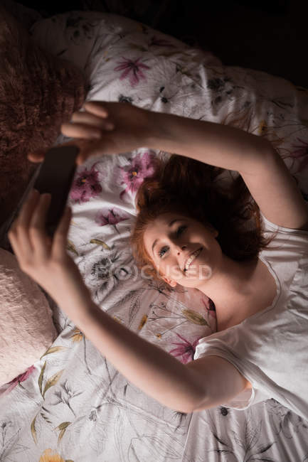 Mujer tomando selfie con teléfono móvil en el dormitorio en casa - foto de stock