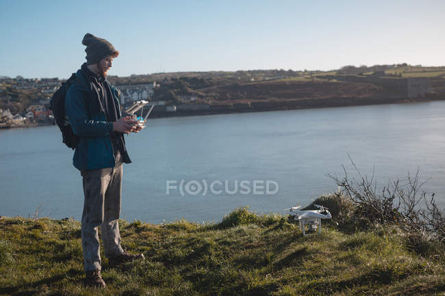Homme randonneur opérant drone près du lac à la campagne — Photo de stock