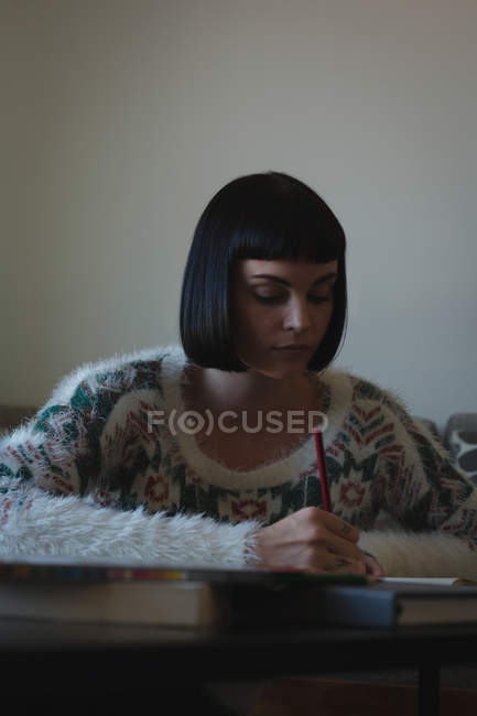 Donna che scrive su un libro in salotto a casa — Foto stock