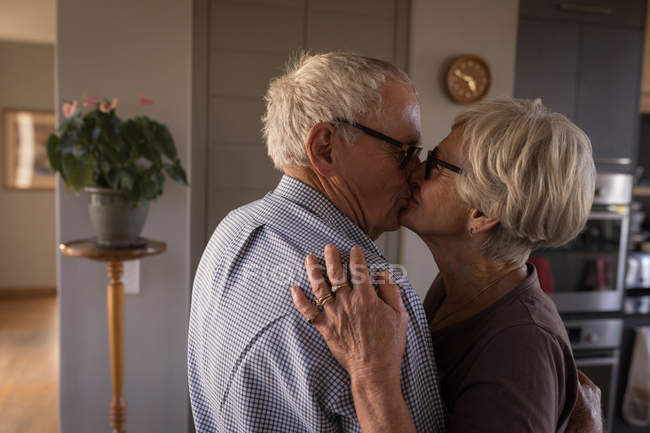 Пожилая пара целуется дома на кухне — стоковое фото