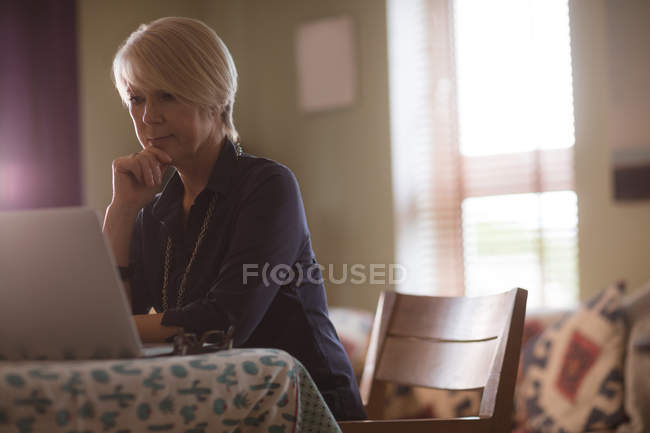 Задумчивая зрелая женщина использует ноутбук дома — стоковое фото