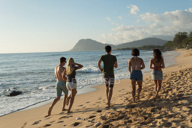 Група друзів біжить на пляжі в сутінках — стокове фото