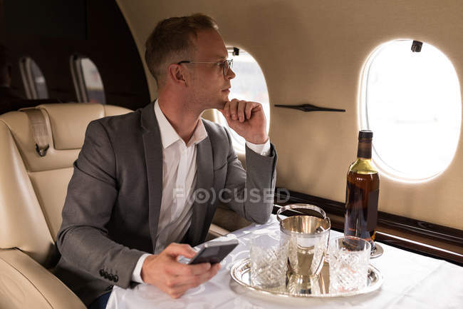 Homme d'affaires réfléchi utilisant le téléphone mobile en jet privé — Photo de stock