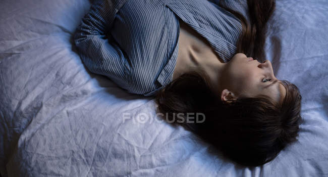 Mulher pensativa deitada na cama no quarto — Fotografia de Stock